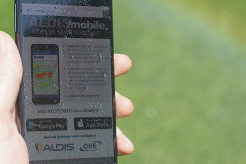 Smartphone mit ALDISmobile App und Regenbogen im Hintergrund